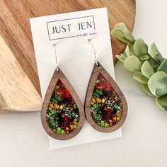 a pair of wooden earrings sitting on top of a piece of paper next to a plant