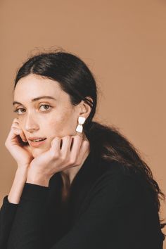 a woman with her hand on her chin, looking at the camera while wearing earrings