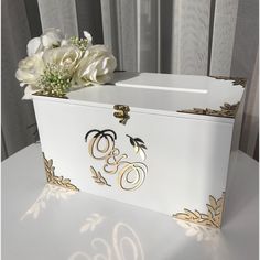 a white and gold box with flowers in it sitting on a table next to a window