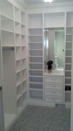 a walk in closet with white shelves and drawers