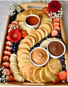 a wooden tray filled with pancakes, fruit and dipping sauce