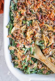 a casserole dish filled with green beans, bacon and other toppings next to a wooden spoon