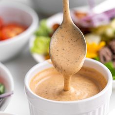 a spoon with dressing being held over a bowl full of salad and other food items