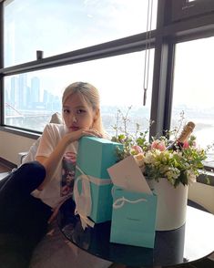 a woman sitting in front of a window holding a blue gift box