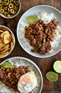 two bowls filled with rice, meat and olives on top of a wooden table