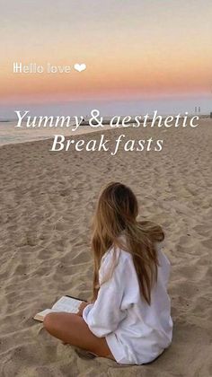 a woman sitting on top of a sandy beach next to the ocean reading a book