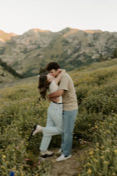 a man and woman kissing in the middle of a field with mountains in the background