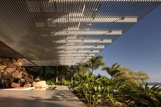 an outdoor area with rocks and plants next to the ocean, under a pergolated roof