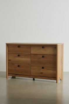 a wooden dresser sitting on top of a floor next to a white wall in an empty room