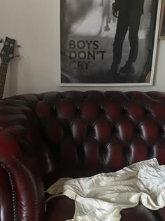 a red leather couch sitting next to a wall with a guitar on top of it