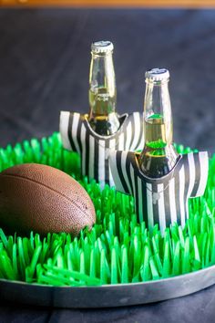 a football and two beer bottles sitting on top of fake grass