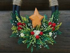 a christmas wreath with red berries, pine cones and white flowers is hanging on a wooden wall