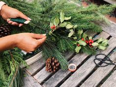 someone is making a christmas wreath out of pine cones and evergreen leaves on a picnic table