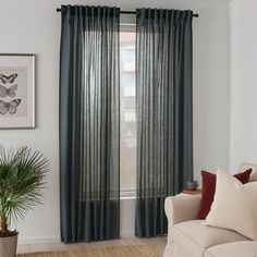 a living room with a couch, chair and window covered in grey sheer curtain panels