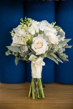 a bouquet of white flowers sitting on top of a wooden table next to a blue wall