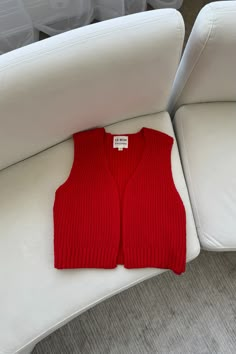 a red sweater vest sitting on top of a white couch next to a plastic container