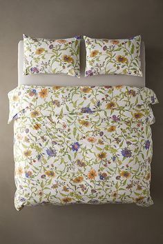 a bed with white sheets and colorful flowers on the pillowcase, in front of a gray wall