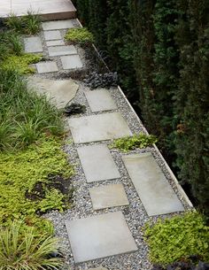 an outdoor walkway made out of stones and gravel surrounded by plants, shrubs and trees