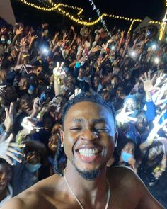 a man is smiling in front of a large group of people at night with their hands up