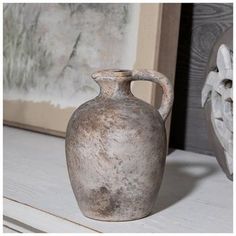 a gray vase sitting on top of a white table next to a framed painting and an old wooden frame