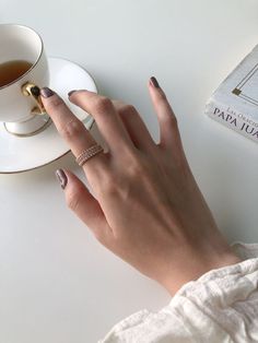 a woman's hand with a ring on it next to a cup of tea