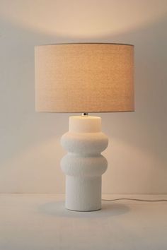 a white table lamp with a beige shade on the base and a light bulb attached to it