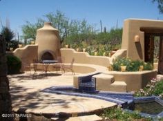 an adobe style house with a fountain and patio furniture in the foreground, surrounded by greenery