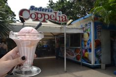 a person holding up a drink in front of a poppetia stand at an amusement park