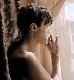 a shirtless man standing in front of a window with his hand on his face