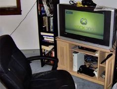 a small tv sitting on top of a wooden stand in front of a black chair