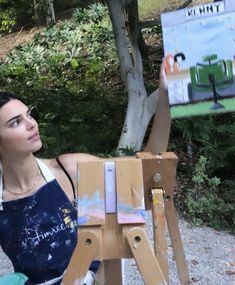 a woman sitting in front of an easel holding up a painting on it's side