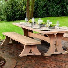 a wooden picnic table set with plates and glasses on it in the middle of a brick patio