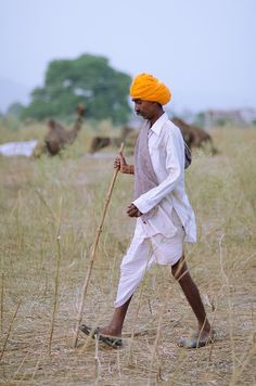 a man with an orange turban is walking in the grass and holding a stick