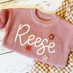 a pink sweater with the word reese on it sitting next to plaid pants and shoes