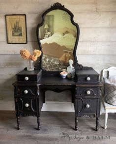 a black vanity with a mirror and flowers in vases on the table next to it