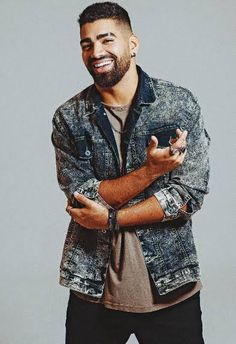 a smiling man with his arms crossed in front of him, wearing a denim jacket and black pants