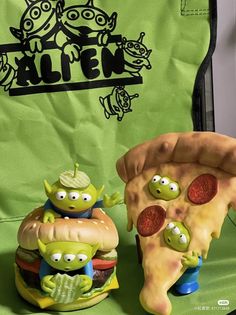 an alien themed pizza and two little green aliens in front of a green bag with alien stickers on it