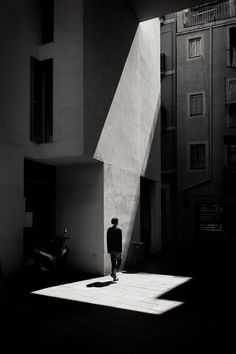 black and white photograph of man standing in front of building with shadows on the ground