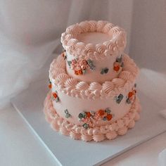 three tiered cake sitting on top of a white tablecloth covered surface with pink frosting