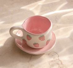 a pink cup and saucer with strawberries on it sitting on a marble table