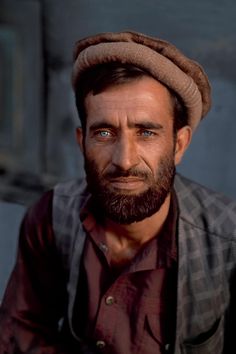 a man with blue eyes and a beard wearing a brown hat is looking at the camera