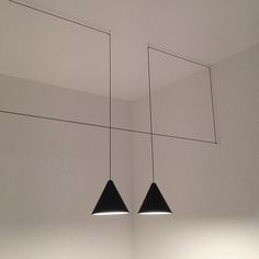 two black lamps hanging from the ceiling in a room with white walls and flooring