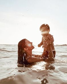 a woman holding a baby in the water with sun shining down on her and behind her