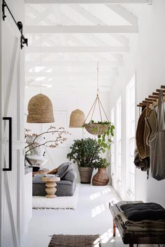 a white hallway with hanging plants and potted plants on the wall next to a bench