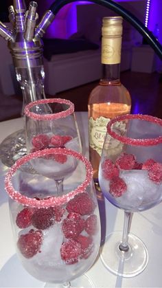 three wine glasses filled with raspberries sit on a table next to a bottle