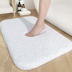 a person standing on top of a white bathroom rug next to a bathtub and toilet