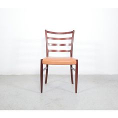 a wooden chair with an orange seat and back rest in front of a white wall