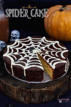 a spider web cake with white icing on a wooden plate next to two pumpkins