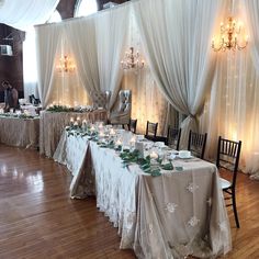 a banquet hall with white drapes and table cloths, decorated with candles and greenery