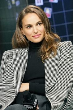 a woman in a black and white jacket is holding a camera while sitting on a chair